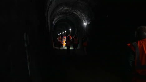 Eine-Gruppe-Von-Menschen-In-Warnwesten-Geht-Durch-Einen-Dunklen-Tunnel-Unter-Der-Erde.