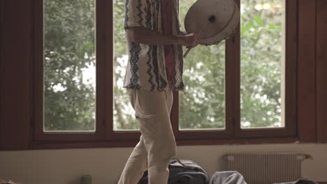 Man-beating-a-handheld-drum-for-sound-healing-ritual-indoors,-closeup