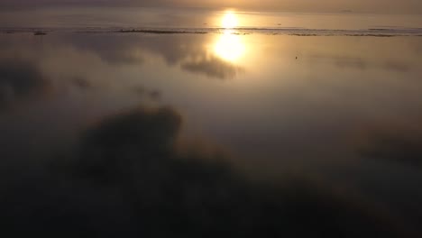 Aerial-drone-view-of-a-empty-beach-at-sunrise,-with-a-reflection-in-the-water,-flying-forward,-tilting-up