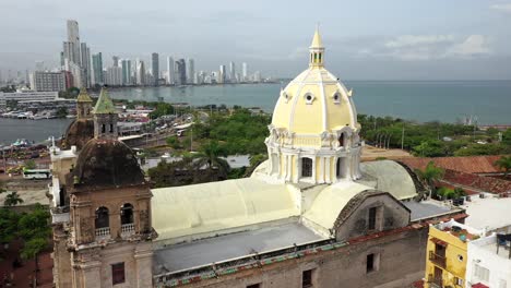 Old-Town-Cartagena-Fly-Over-Aerial-Cinematic-Shot-Showcasing-San-Pedro-Claver-Church-with-Modern-Buildings-in-Bocagrande-as-Backdrop