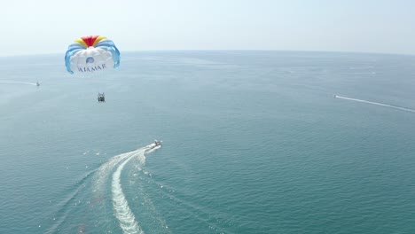 Luftaufnahme-Folgt-Schnellboot,-Das-Farbenfrohes-Parasailing-Auf-Ruhigem-Wasser-Zieht