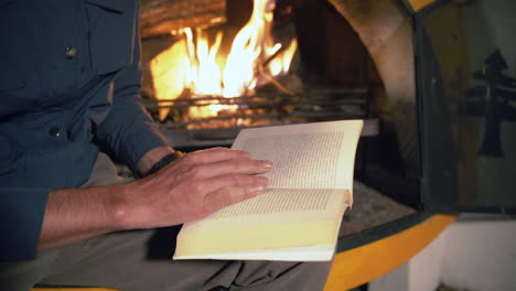 man-finds-solace-and-relaxation-as-he-immerses-himself-in-a-book,-while-the-cozy-warmth-of-a-cabin-fireplace-dances-in-the-background,-creating-a-comforting-and-serene-atmosphere