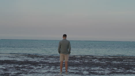 Man-full-of-thoughts-reflecting-stands-alone-in-silence-in-front-of-the-vast-ocean-during-twilight