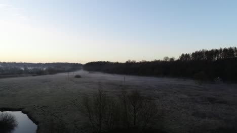 Temprano-En-La-Mañana,-El-Sol-Está-Saliendo-Sobre-El-Pueblo-Donde-Hay-Un-Ferrocarril-Que-Atraviesa-El-Pueblo-Cerca-De-Un-Campo-Vacío-Cubierto-De-Niebla-Y-Escarcha-Sobre-La-Hierba.