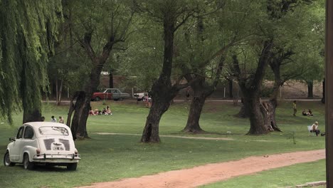 Gimbal-shot-of-people-in-park-and-old-Fiat-parked-on-grass