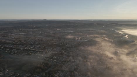 Wide-angle-drone-footage-over-Folsom,-USA-on-a-bright-early-morning,-with-misty-clouds-moving-in-from-the-right