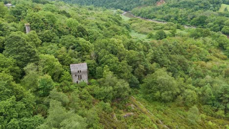 Rising-aerial-view-of-old-tin-and-copper-mines-along-the-banks-of-the-river-Tamar-in-Cornwall,-highlighting-historical-industrial-ruins