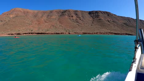 Una-Lancha-Motora-Navega-Junto-A-Un-Grupo-De-Turistas-En-Kayak-Remando-En-Aguas-De-Color-Azul-Verdoso-Al-Pie-De-Una-Montaña-Tropical.