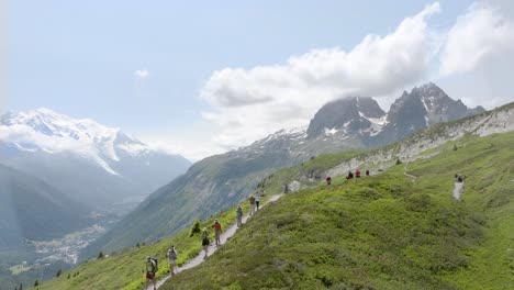 Excursionistas-Cruzando-Los-Prados-Alpinos-En-El-Tour-Du-Mont-Blanc,-Con-Impresionantes-Vistas-A-Las-Montañas-Al-Fondo