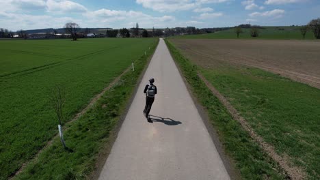 Vista-Aérea-De-Un-Hombre-Conduciendo-Un-Scooter-Eléctrico-En-Una-Pintoresca-Carretera-Rural,-Cerca-De-Svitavy-En-La-República-Checa