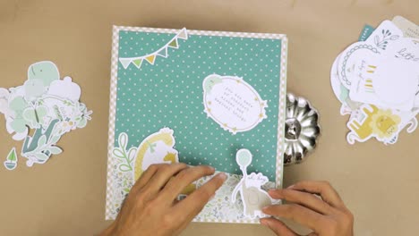 Creating-cute-scrapbook-baby-album-cover-with-decorative-paper-cutouts-and-embellishments