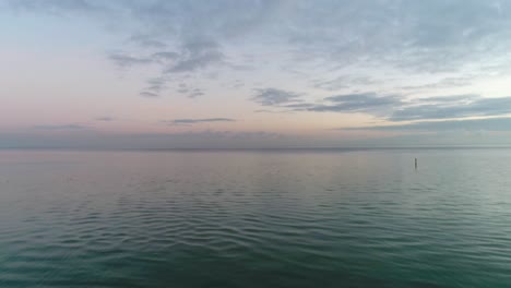 Drone-flying-over-Beach-shore-and-Calm-blue-tranquil-bay-with-Soft-clouds-in-horizon