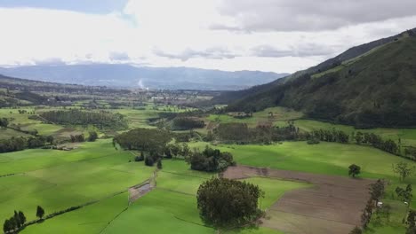 Green-agriculture-fields-in-between-mountain-ranges,-aerial-drone-view