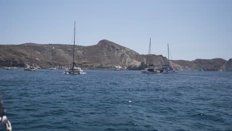 Toma-En-Cámara-Lenta-De-Un-Catamarán-Explorando-La-Costa-De-Santorini-Durante-El-Verano