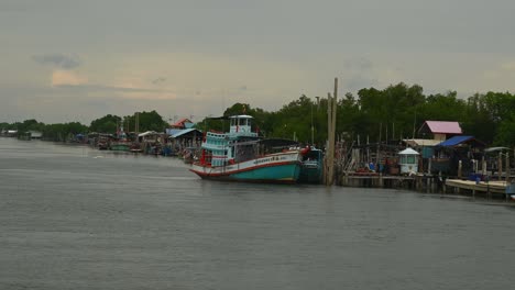 A-touring-Thai-boat-on-the-right-side-of-the-estuarine-ready-to-go-out-the-the-ocean,-piers-and-boats-are-also-revealed,-a-community-of-seamen-and-fishermen