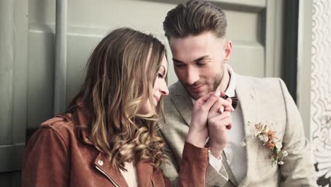 Retro-styled-wedding-couple-in-brown-leather-jacket-leaning-at-a-grey-container-while-groom-is-kissing-and-holding-brides-hand-gently,-softly-and-passionate