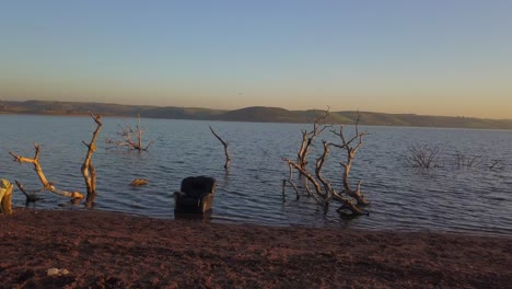 A-chair-in-the-ocean-surrounded-by-branches-during-a-sunset-on-a-beach,-orbit-shot