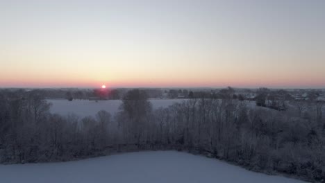 Dolly-Vorwärts-über-Ein-Schneebedecktes-Feld-Und-Bäume-In-Richtung-Der-Sonne,-Die-Am-Horizont-Aufgeht