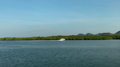 Panning-shot-of-bright-white-boat-speeding-next-to-an-island-in-Thailand