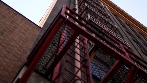 Vista-Panorámica-Lenta-De-Un-Edificio-Histórico-Industrial-Clásico-Que-Muestra-Su-Hermoso-Sistema-De-Escalera-De-Incendios-De-Color-Rojo-Desde-El-Piso-Del-Nivel-Del-Suelo.