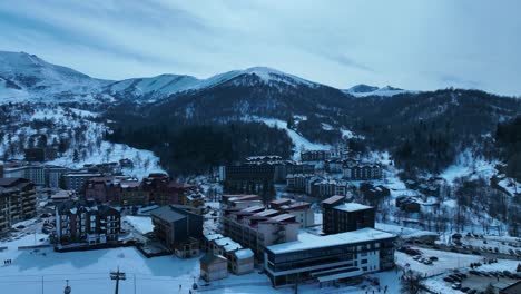 Vista-Aérea-De-Un-Centro-Invernal,-Con-Edificios-Cubiertos-De-Nieve-Y-Un-Pintoresco-Entorno-Montañoso.