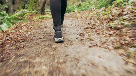 A-young-woman-wearing-a-bright-yellow-jacket-walks-through-a-green-mossy-forest,-close-up-tracking-shot-of-her-boots