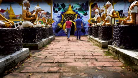 Pareja-Caminando-Hacia-La-Entrada-De-Wat-Bang-Chak-Pasando-Por-Estatuas-Sentadas