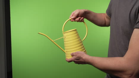 Yellow-watering-can-poured-by-adult-man-in-front-of-chroma-green-screen