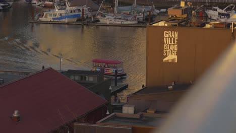 Panoramic-shot-of-the-Granville-Island-Water-Taxi-at-dusk-doing-its-regular-tour-with-its-calm-surrounding-waters-and-the-cityscape-in-the-background