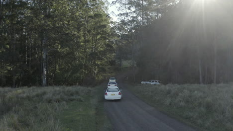 4k-Drone-shot-of-three-white-cars-driving-through-a-beautiful-tropical-forest-in-Australia