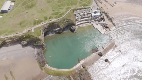 Eine-Drohnenaufnahme-Des-Bude-Sea-Pools-In-Bude,-Cornwall,-Zeigt-Das-Klare-Blaue-Wasser,-Die-Umliegenden-Felsklippen-Und-Den-Strandbereich.