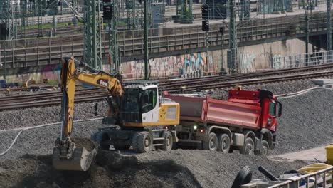 Excavator-digging-and-loading-gravel-onto-truck-in-front-of-railways-Stuttgart-21