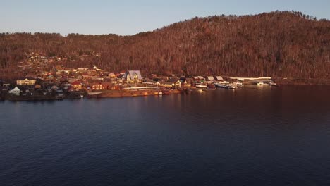 Nikola-a-small-Russian-town-by-mountain-foothill-on-Angara-river-banks,-aerial-shot