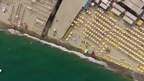 A-beach-in-liguria,-italy-with-rows-of-yellow-sunbeds-and-turquoise-sea,-aerial-view