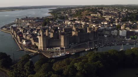 Aerial-footage-of-Caernarfon-Castle-shot-by-a-Drone-in-evening-light,-also-showing-the-Menai-Straits,-Gwynedd,-North-Wales,-UK