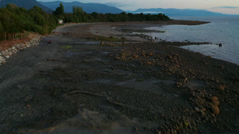 Aerial-dolly-shot-over-a-rocky-coastal-beach-with-a-quad-bike-riding-in-shot,-evening-sunlight