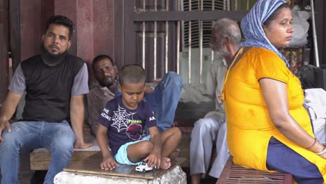 Little-Indian-boy-playing-with-car-toy-sitting-on-a-streetside-corner-with-family-members