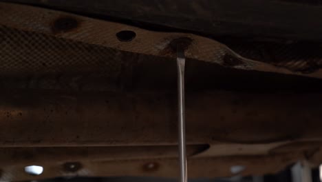 A-mechanic-using-a-screwdriver-to-loosen-a-damaged-screw-under-a-vehicle