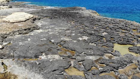 Aerial-forward-view-of-Rocky-Limestone-Beach-in-Sliema,-Malta,-Tilt-Up