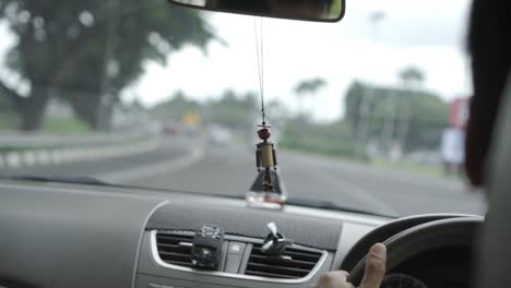 Car-cruising-down-road-in-Jakarta,-Indonesia-with-minifan-hooked-onto-air-conditioner-vent