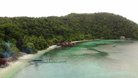 Aerial-view-of-Kri-Island,-Raja-Ampat,-Indonesia,-showing-stilt-huts-along-a-pristine-beach