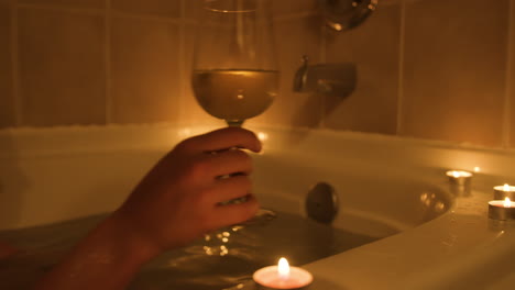 Young-woman-reaches-for-glass-of-wine-while-taking-a-warm-relaxing-bath