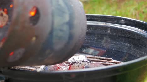 Blazing-hot-coal-stored-in-chimney-container-being-poured-into-the-bowl-shaped-grill