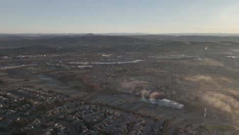 Wide-angle-drone-Birdseye-footage-over-city-in-Central-Valley-in-California,-USA-on-a-sunny-misty-morning,-with-mountains-in-the-distance