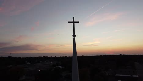 Drone-orbit-around-cross-on-a-church-steeple-with-a-gorgeous-sunset-over-the-city-skyline