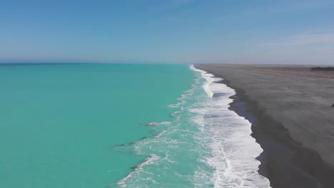 Malerische-Drohnenansicht-Der-Küstenlinie-Des-Türkisfarbenen-Ozeans-Und-Des-Dunklen-Sandstrands-Neuseelands-In-4K-An-Einem-Klaren,-Sonnigen-Tag