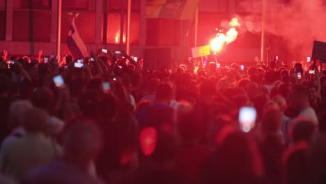 Protesters-With-Flags,-Smartphones,-And-Firework-At-Night