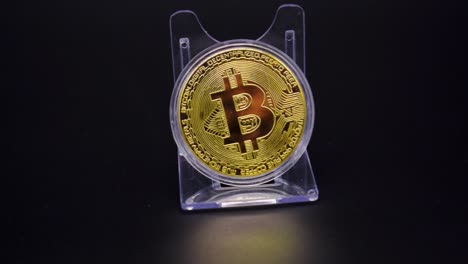 Close-Up-Of-Physical-Golden-Bitcoin-In-Plastic-Shelf-On-A-Black-Background