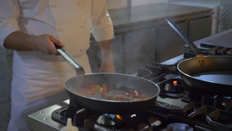 A-chef-in-the-kichten-cooking-and-mixing-peppers-with-a-big-flame,-close-up