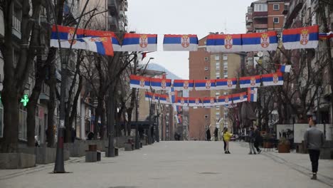 Personas-En-La-Zona-Peatonal-Del-Norte-De-Mitrovica,-Con-Muchas-Banderas-Serbias